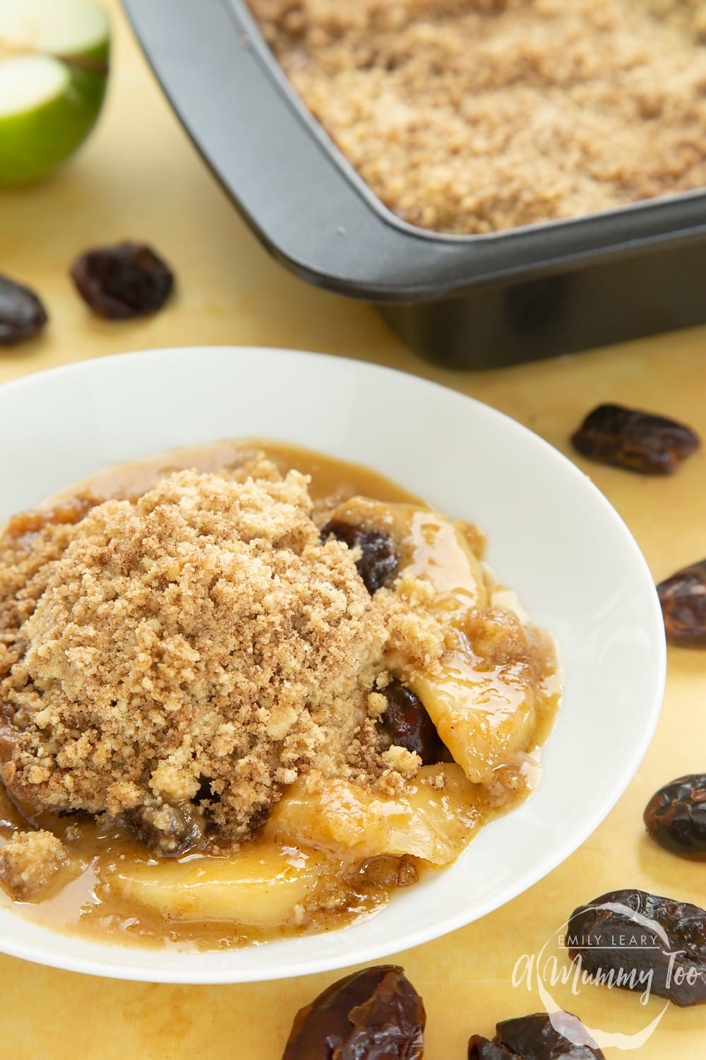 Side shot of a plate of toffee apple crumble on a yellow table. 