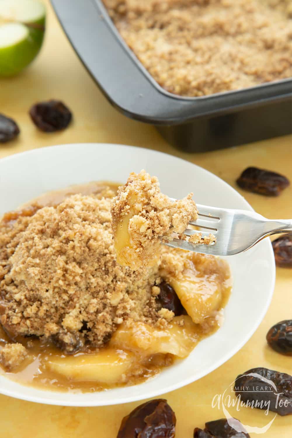 A fork pulling out some of the toffee apple crumble off from the plate below. 