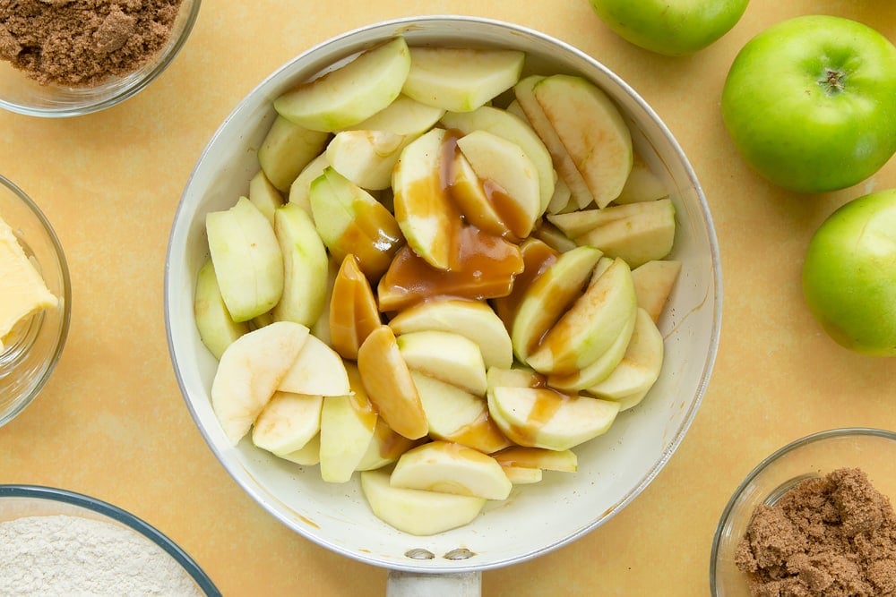 Adding sliced apples to the pan for toffee apple crumble. 