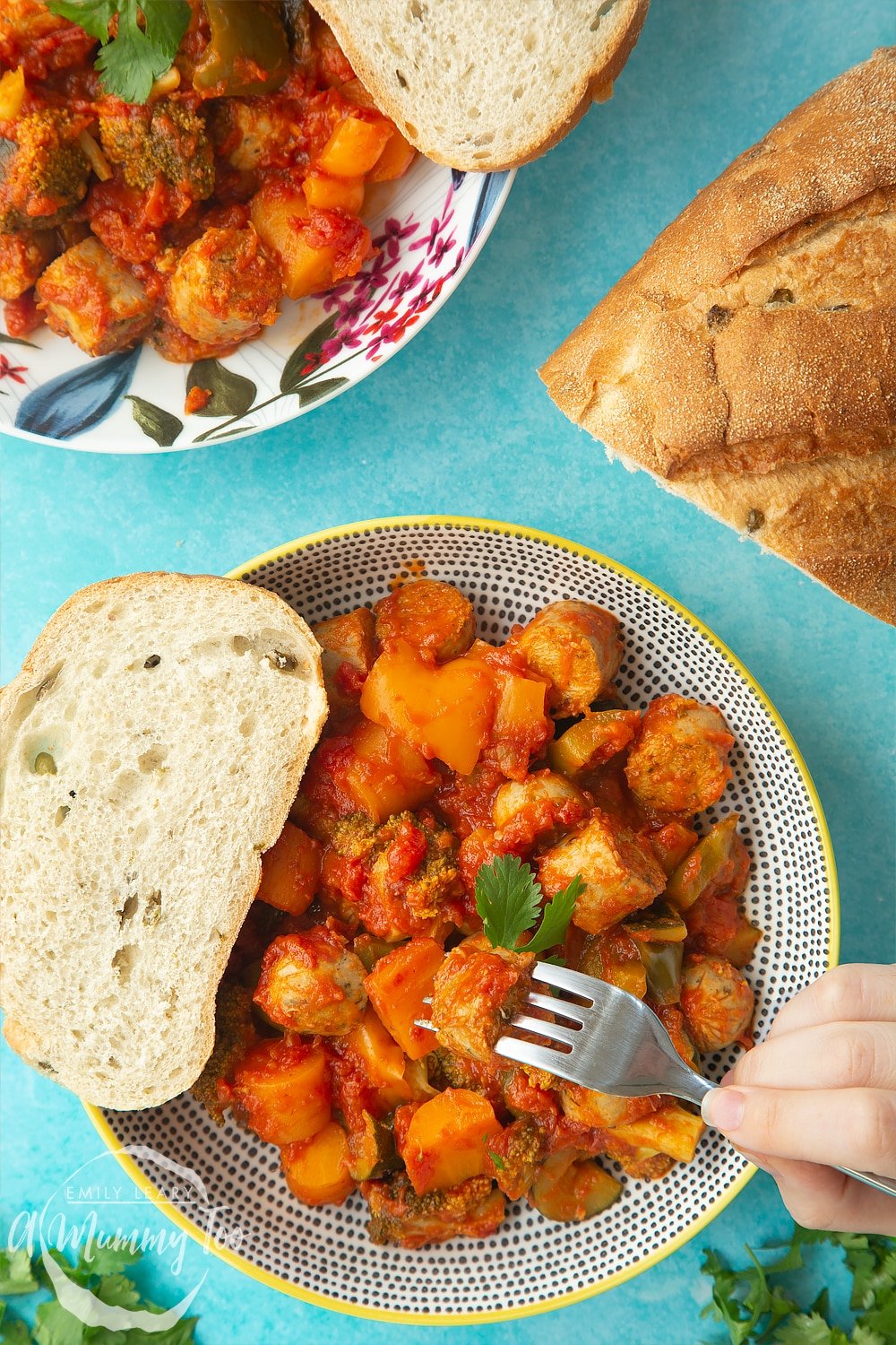 Overhead shot of two decorative bowls filled with slow-cooked vegetarian sausage casserole. At the side of the bowls there's a crusty bread roll. 