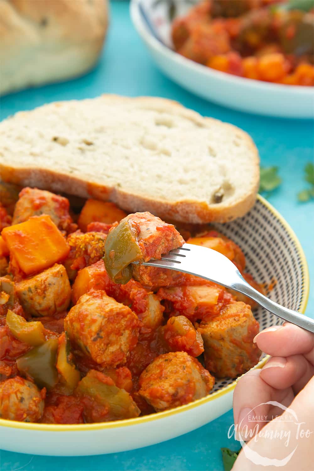 A fork picking up some slow-cooked vegetarian sausage casserole out of a decorative bowl.