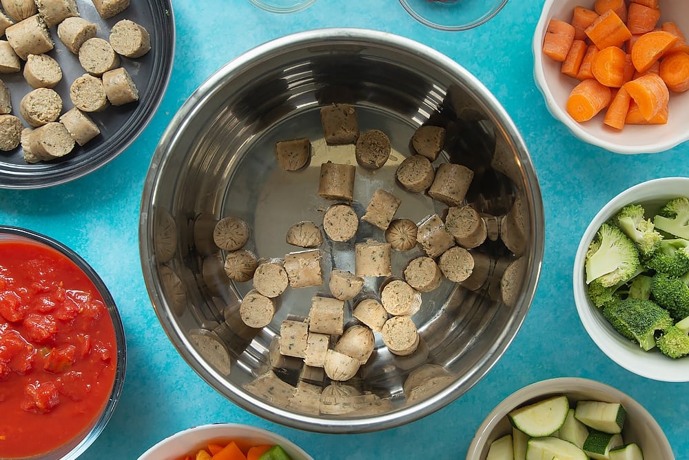 Overhead shot of chopped up sausage for the Slow-cooked vegetarian sausage casserole surrounded by other ingredients required for the meal. 