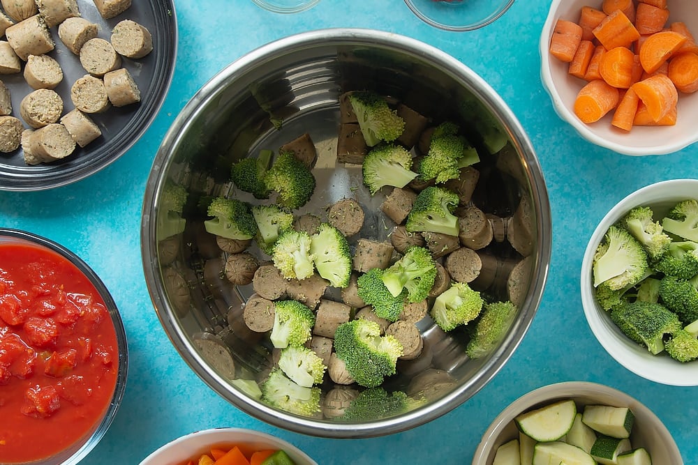 Adding the broccoli to the bowl for the slow-cooked vegetarian sausage casserole. Additional ingredients for the recipe surround the bowl. 