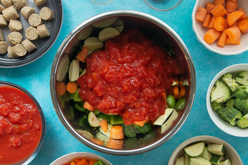 Adding chopped tomatoes to the bowl of Slow-cooked vegetarian sausage casserole ingredients ready for the slow cooker.