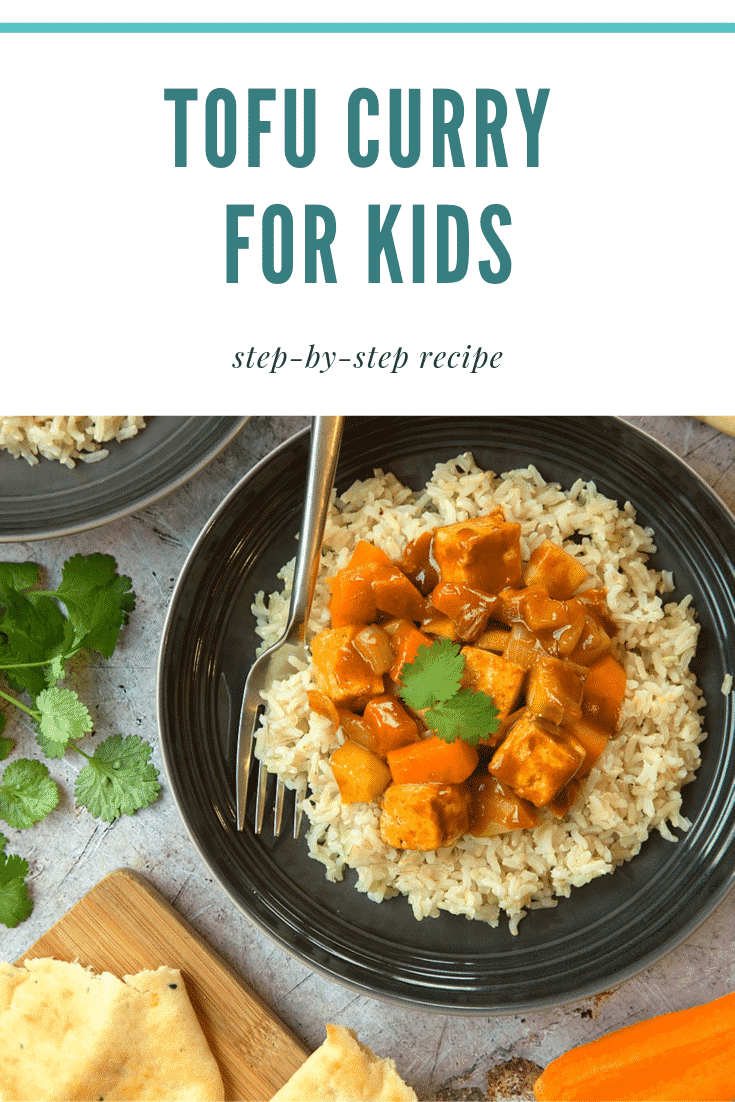 Overhead shot of the tofu curry for kids on a black plate with a fork on the side. The plate is surrounded by some additional ingredients required for the recipe. 