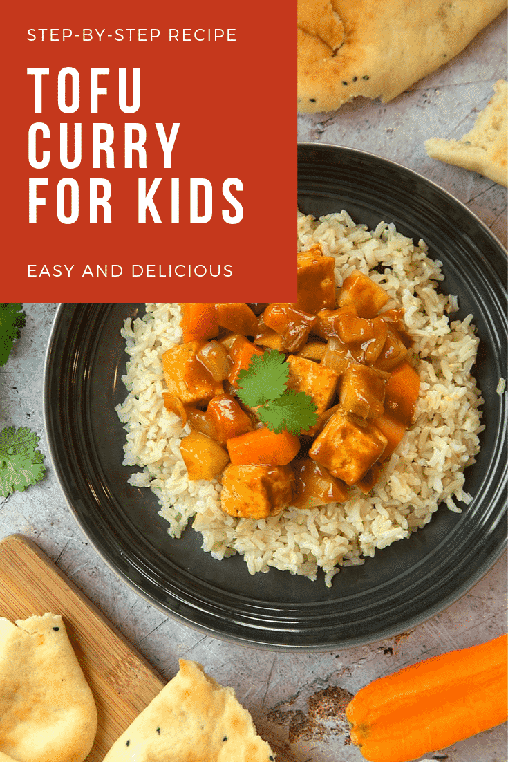 Overhead shot of the tofu curry for kids on a black plate with a fork on the side. The plate is surrounded by some additional ingredients required for the recipe. At the top of the image there's some text describing the image for Pinterest.