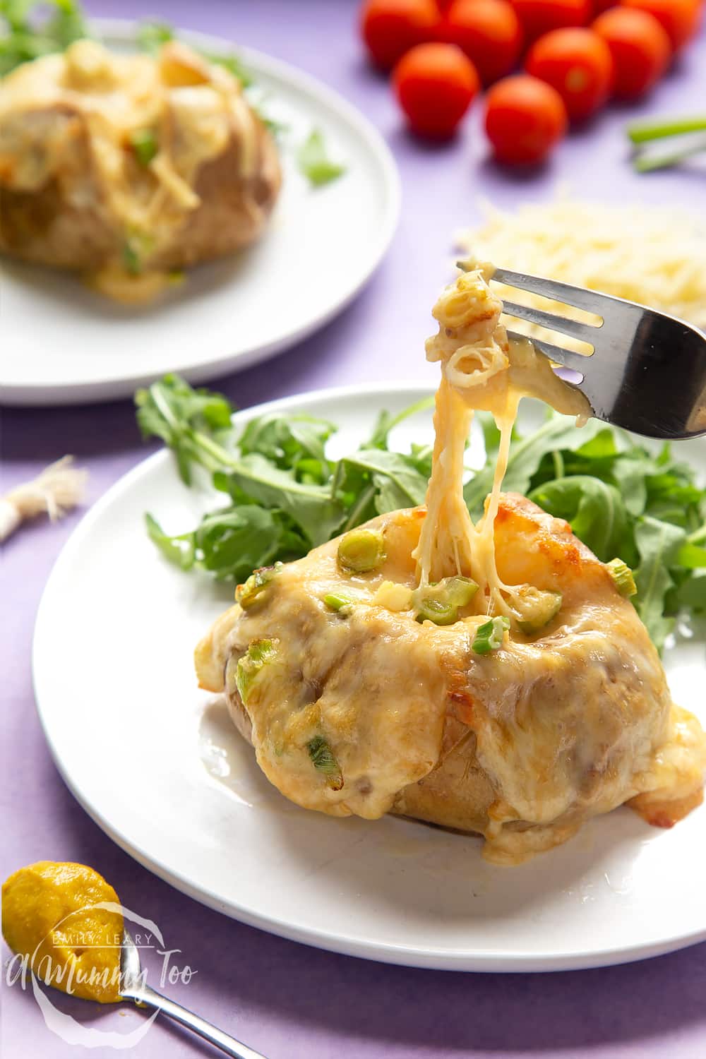 A cheese and onion jacket potato served on a white plate with rocket. A fork stretches the cheese from the potato.