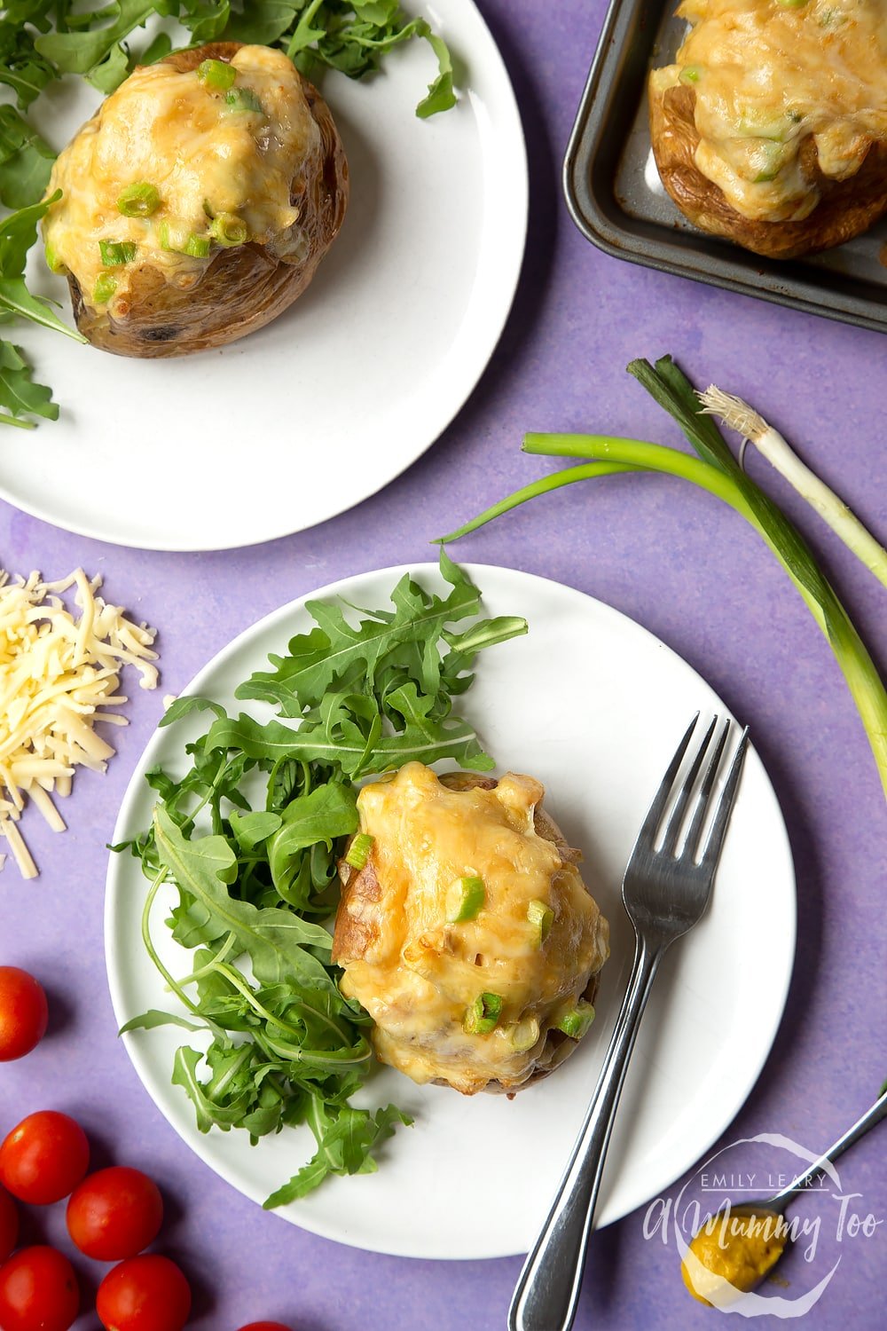 A cheese and onion jacket potato served on a white plate with rocket. A fork rests to the side.