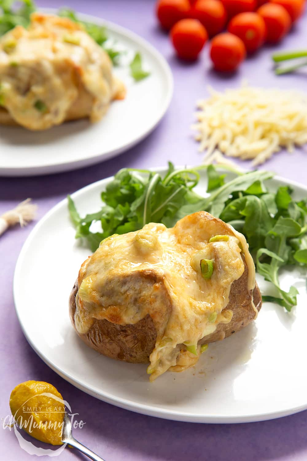 A cheese and onion jacket potato served on a white plate with rocket. The cheesy topping is dripping down the sides of the potato.