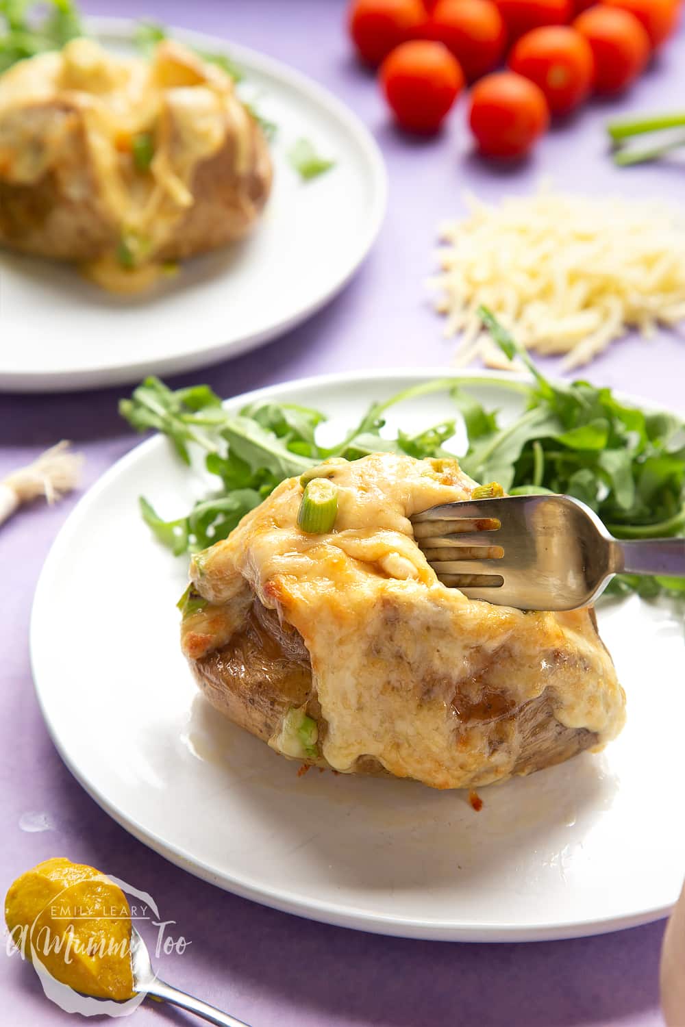 A cheese and onion jacket potato served on a white plate with rocket. A fork digs into the potato.