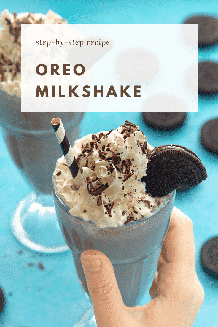 A hand holding an oreo milkshake topped with whipped cream and an oreo cookie. There's an additional milkshake and some oreo cookies on the light blue table in the background. At the top of the image there's some text describing the image for Pinterest. 