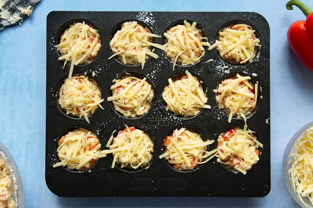 Topping the cheese and red pepper muffins in muffin cases with additional cheese.
