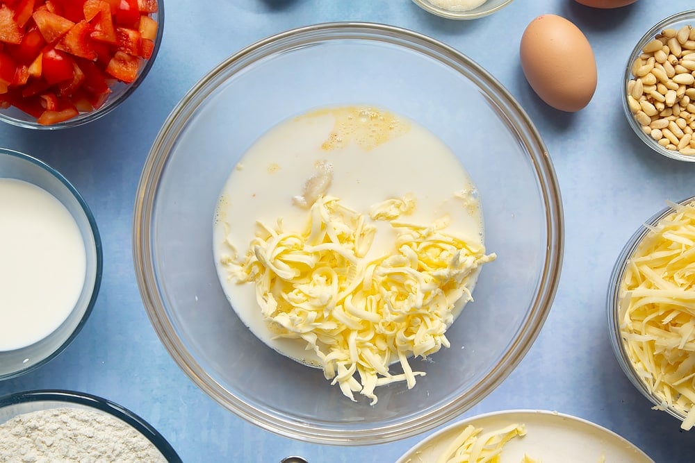 Adding in butter and grated cheese to a bowl to make the cheese and red pepper muffins. At the side there's a number of bowls filled with ingredients for the recipe. 