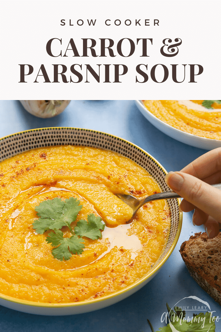 Hand holding a spoon going into a bowl of slow cooked carrot and parsnip soup.