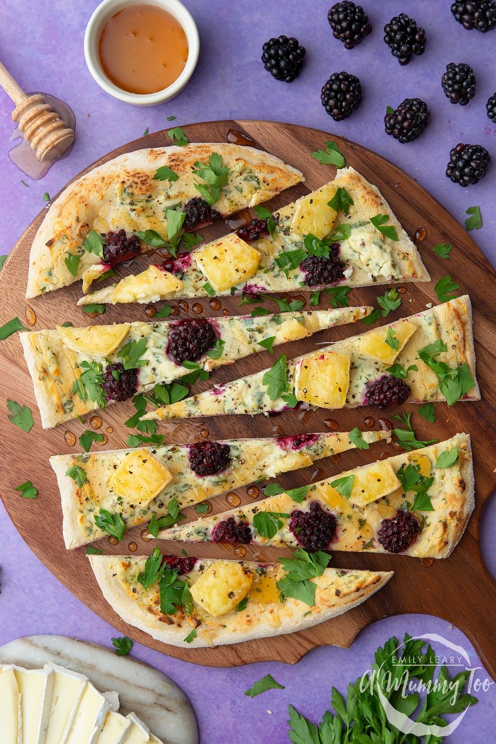 Brie and blackberry pizza sliced on a dark wooden board. 