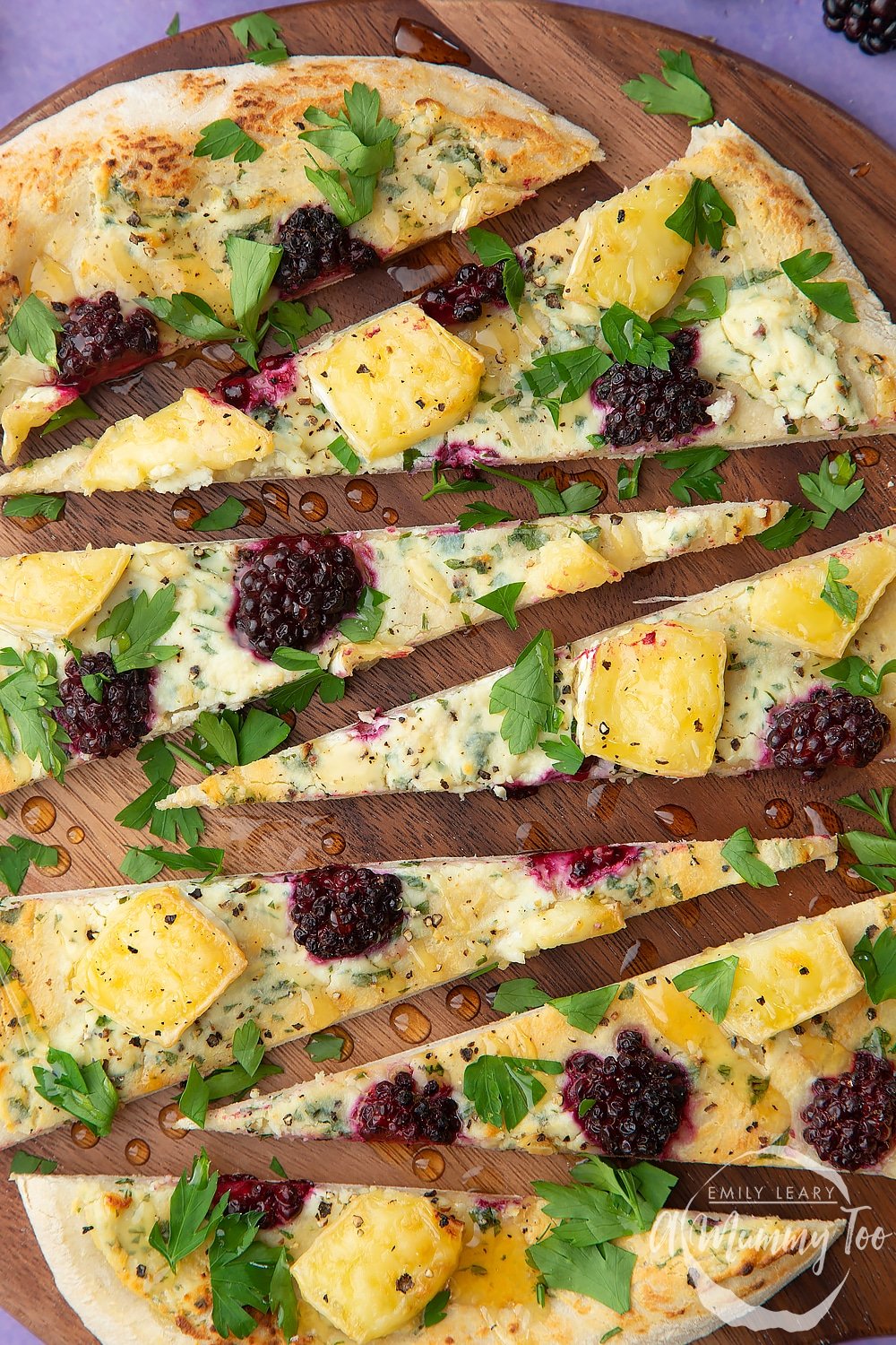 Brie and blackberry pizza sliced on a dark wooden board. The pizza has been drizzled with honey.