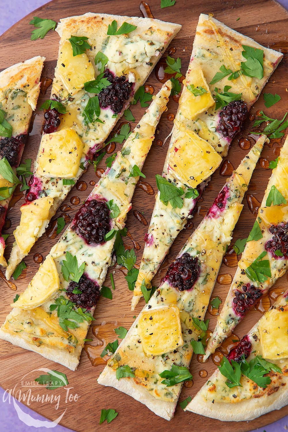 Brie and blackberry pizza sliced on a dark wooden board. The slices are long and thin.