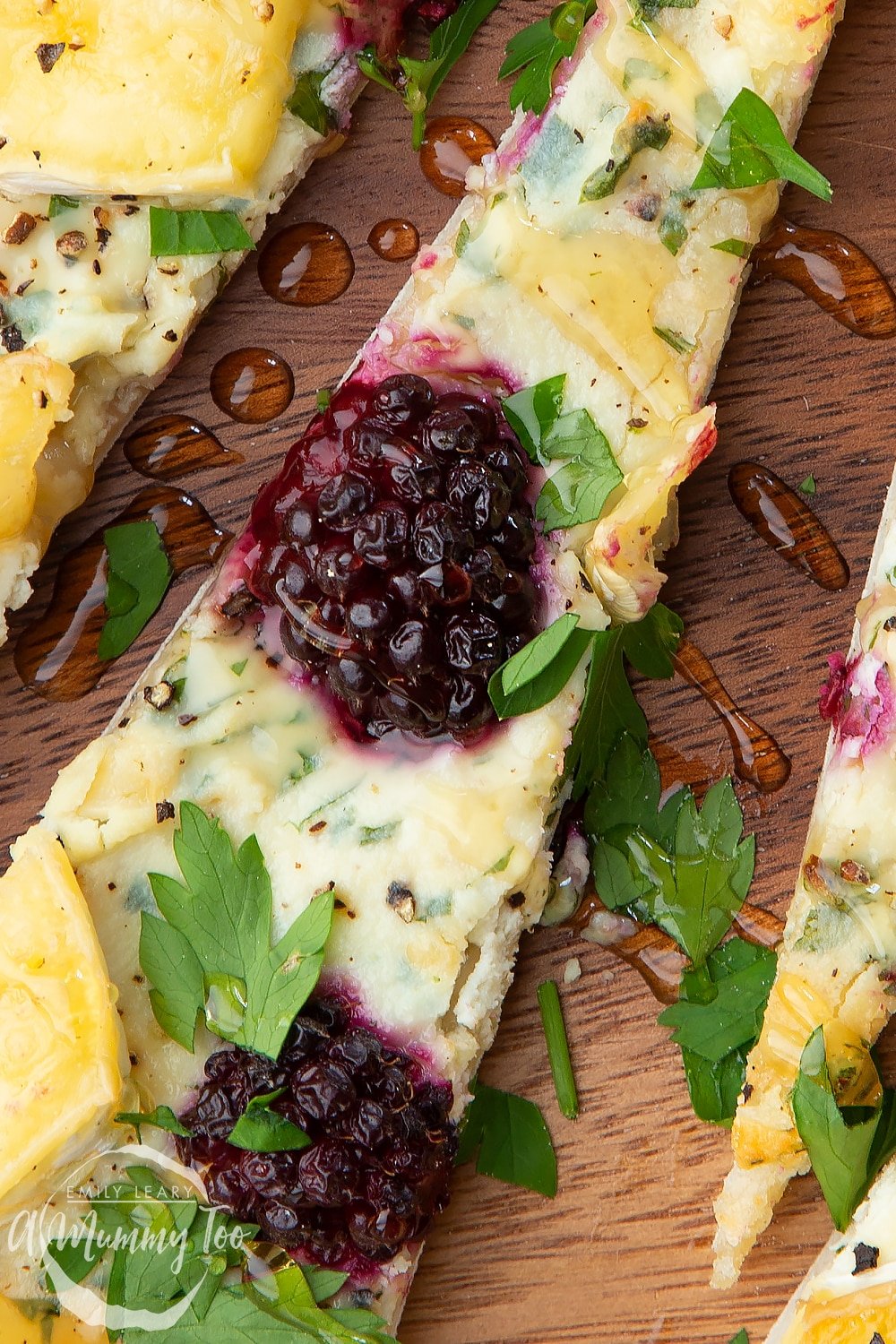 Closeup of a brie and blackberry pizza, sliced on a dark wooden board. 