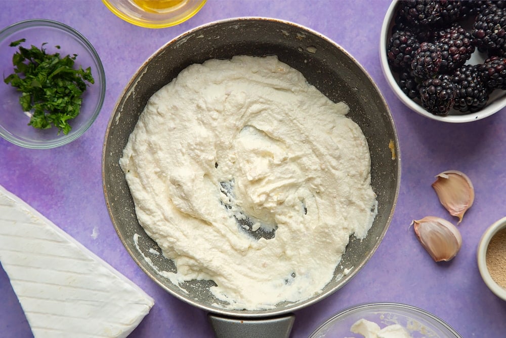 Ricotta whipped with garlic in a small frying pan. Ingredients for brie and blackberry pizza surround the pan.