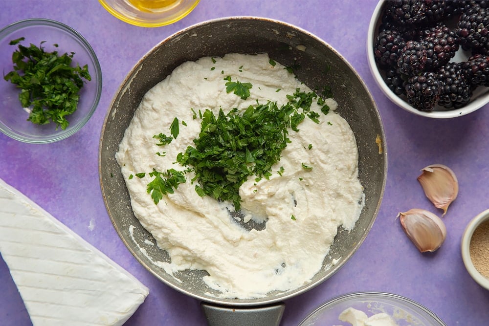 Ricotta whipped with garlic in a small frying pan, topped with parsley. Ingredients for brie and blackberry pizza surround the pan.