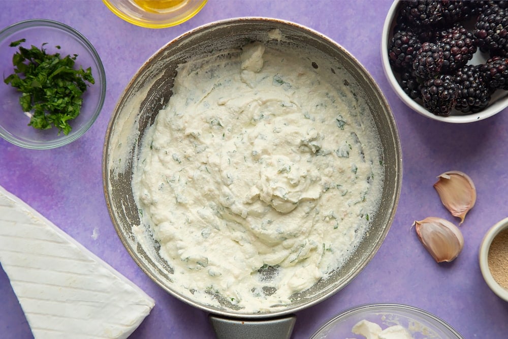 Ricotta whipped with garlic and parsley in a small frying pan. Ingredients for brie and blackberry pizza surround the pan.