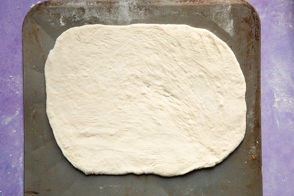 An oblong of pizza base on a baking sheet. 