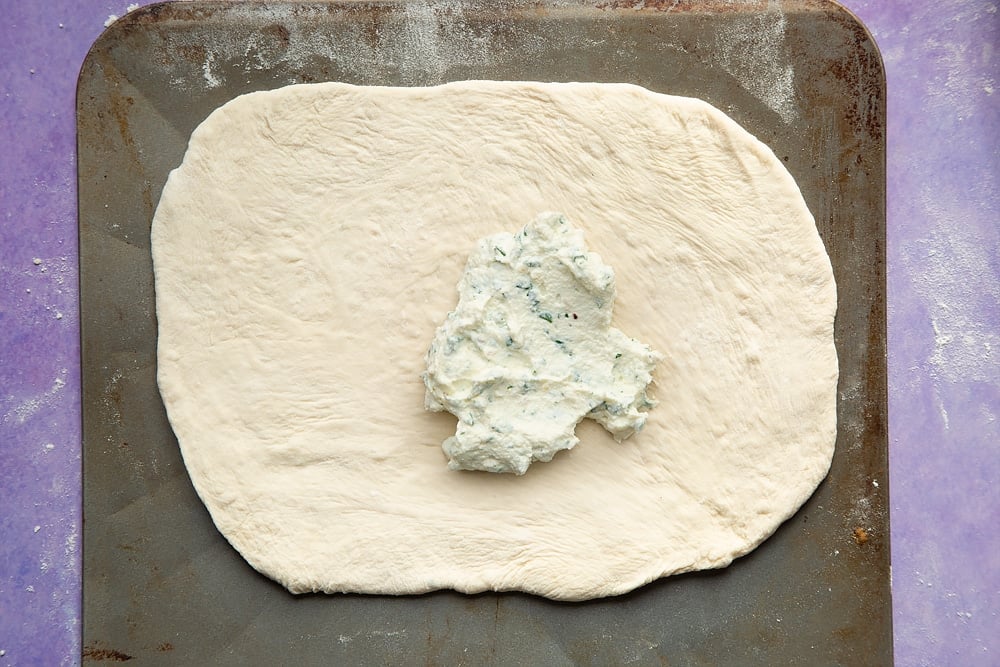 An oblong of pizza base on a baking sheet, spread with the ricotta mix. 