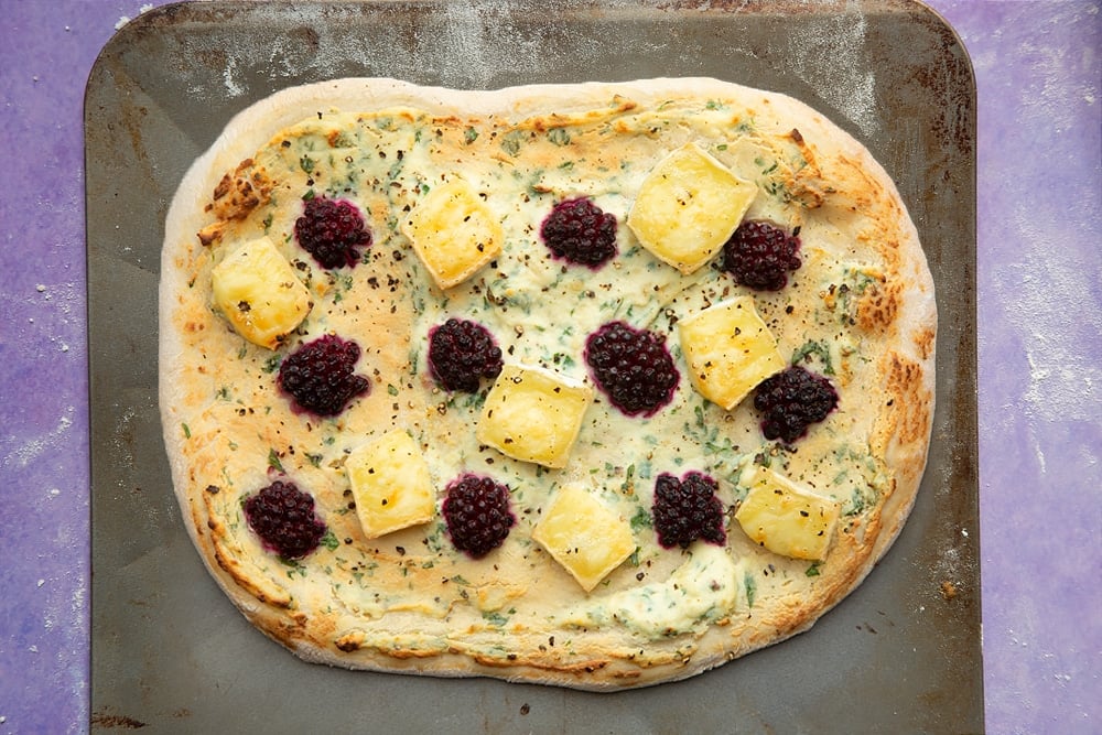 A freshly baked brie and blackberry pizza with a golden crust on a baking sheet.