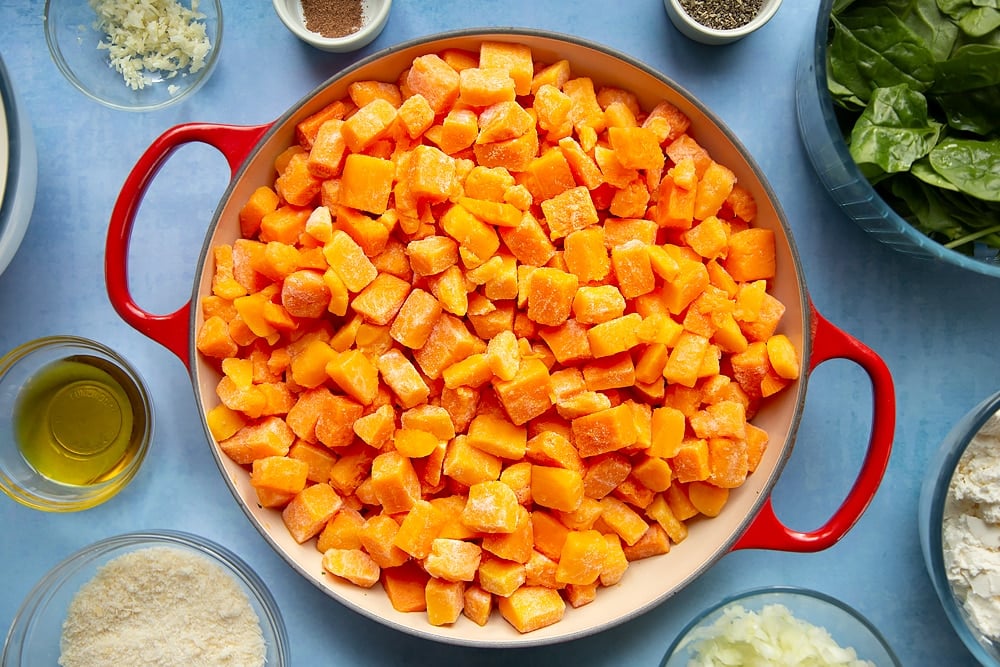 Overhead shot of chopped butternut squash in a large red pan
