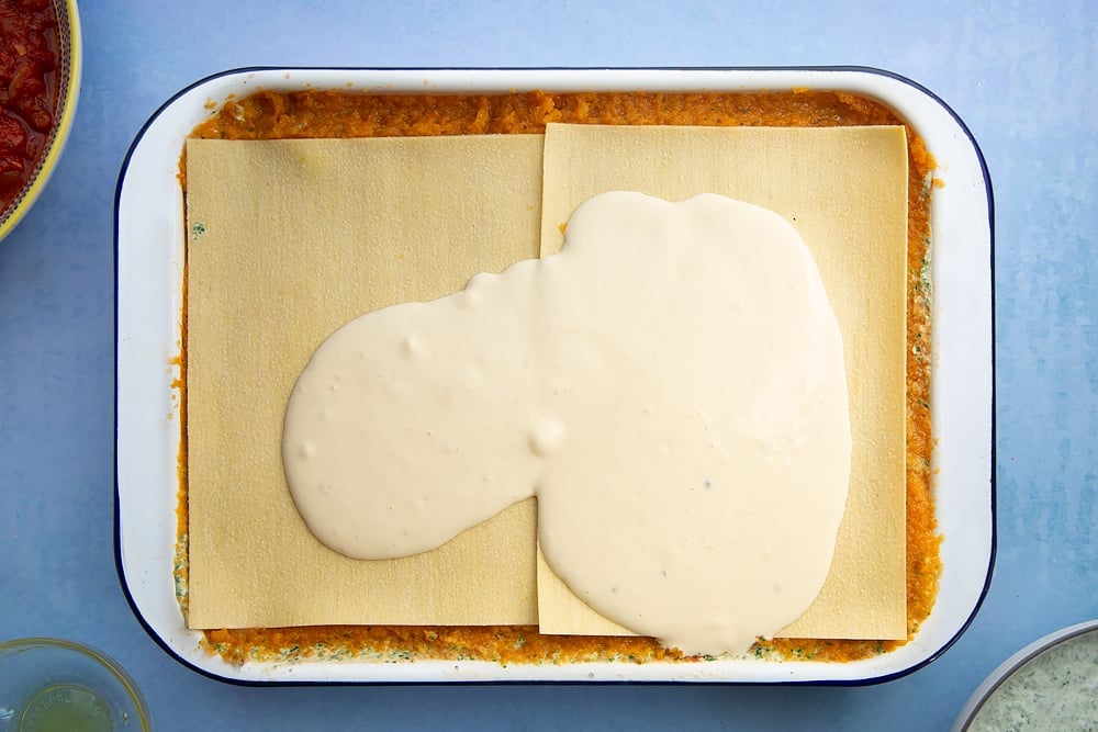 Overhead shot of white sauce on top of lasagne sheets in a lasagne dish