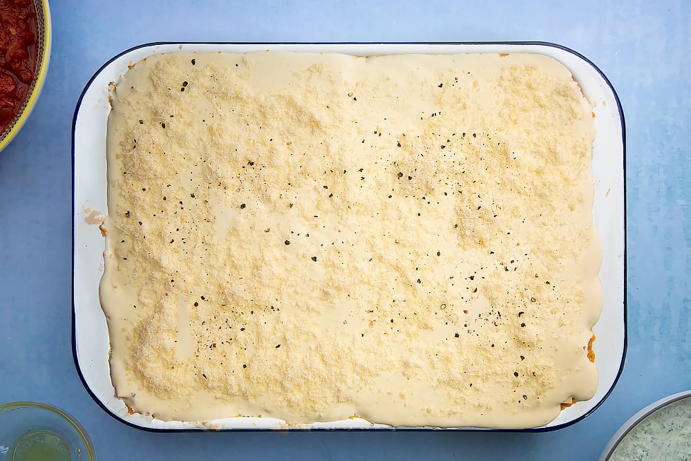 Overhead shot of Parmesan on top of a white sauce in a lasagne dish