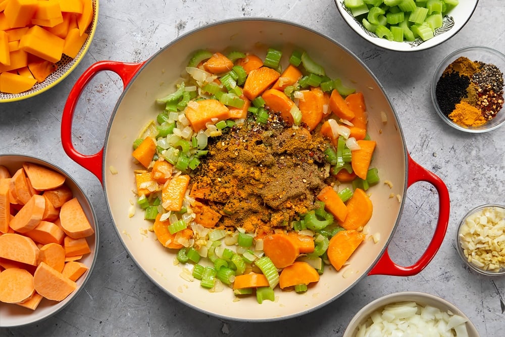 Adding the coriander, cumin, garam masala, madras powder, chilli flakes, black onion seeds, black pepper, turmeric and salt to the pan with the pre-fried ingredients and turning it down to a medium heat.