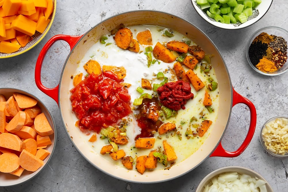 Adding tomato paste, chopped tomatoes, coconut milk and sweet chilli sauce to the butternut squash and chickpea curry pan. 