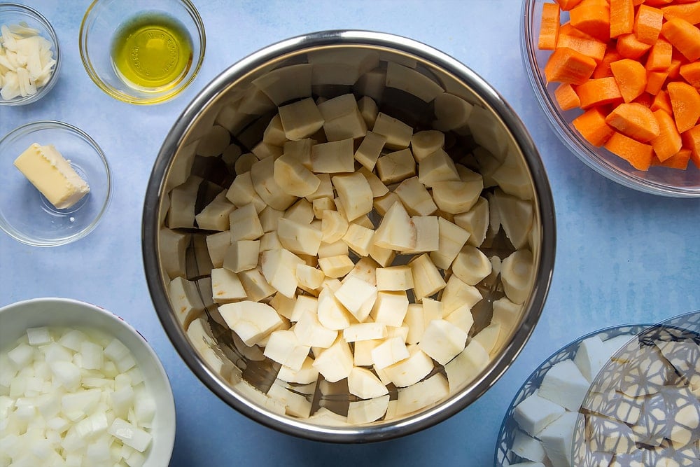 Bowls and pans filled with the ingredients needed to make a delicious carrot and parsnip soup.