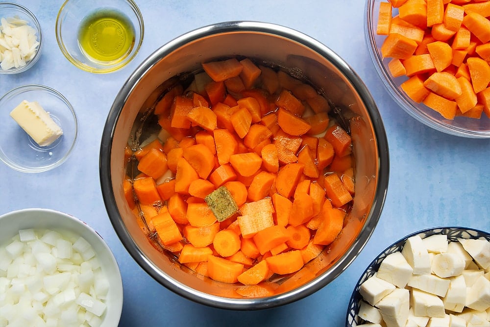 Adding water and a stock cube to the pan filled with the ingredients required for carrot and parsnip soup.