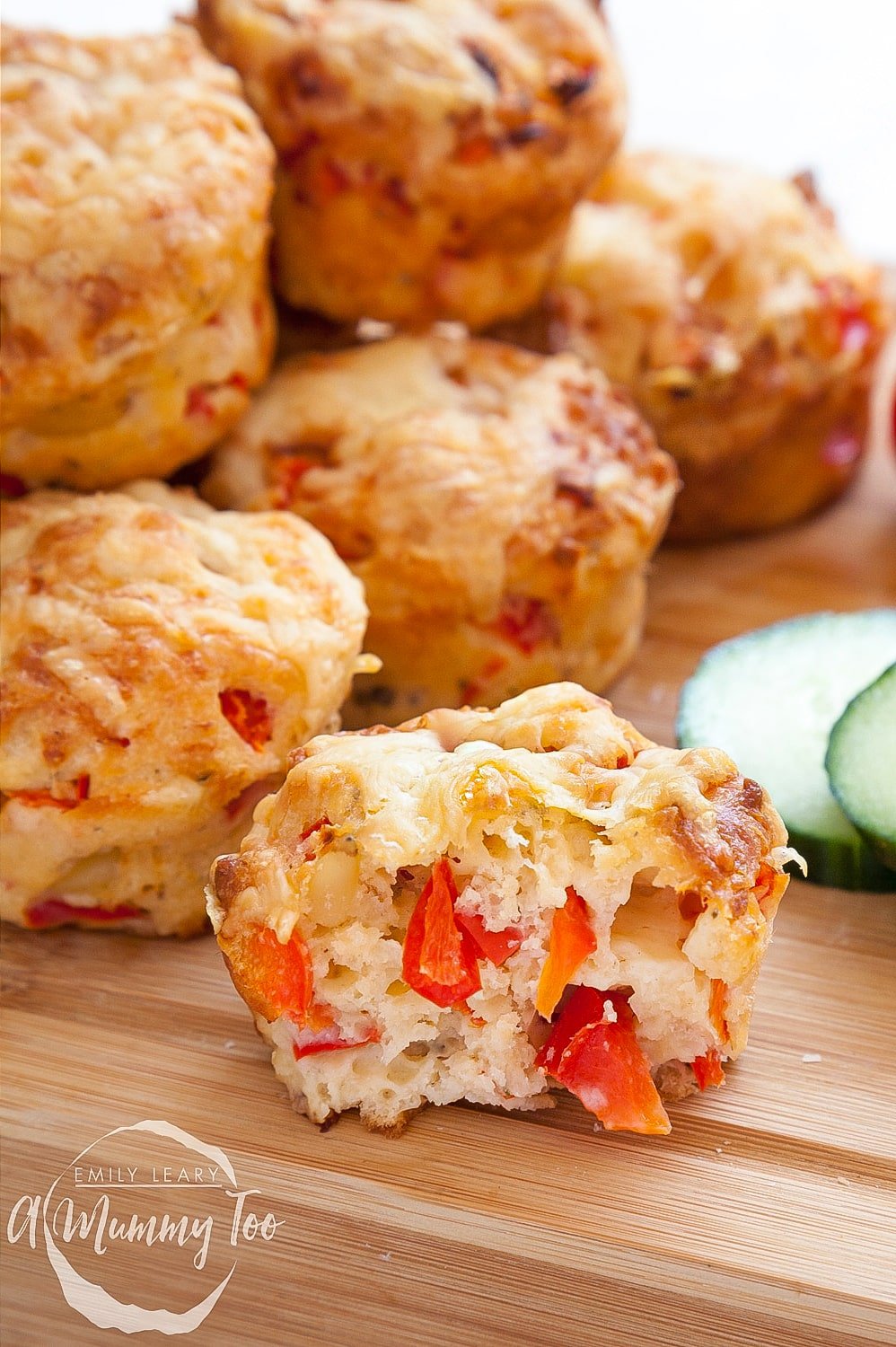 Close up of the inside of one of the cheese and red pepper muffins having been cooked in the oven. The background shows more cheese and red pepper muffins stacked on top of one and other. 