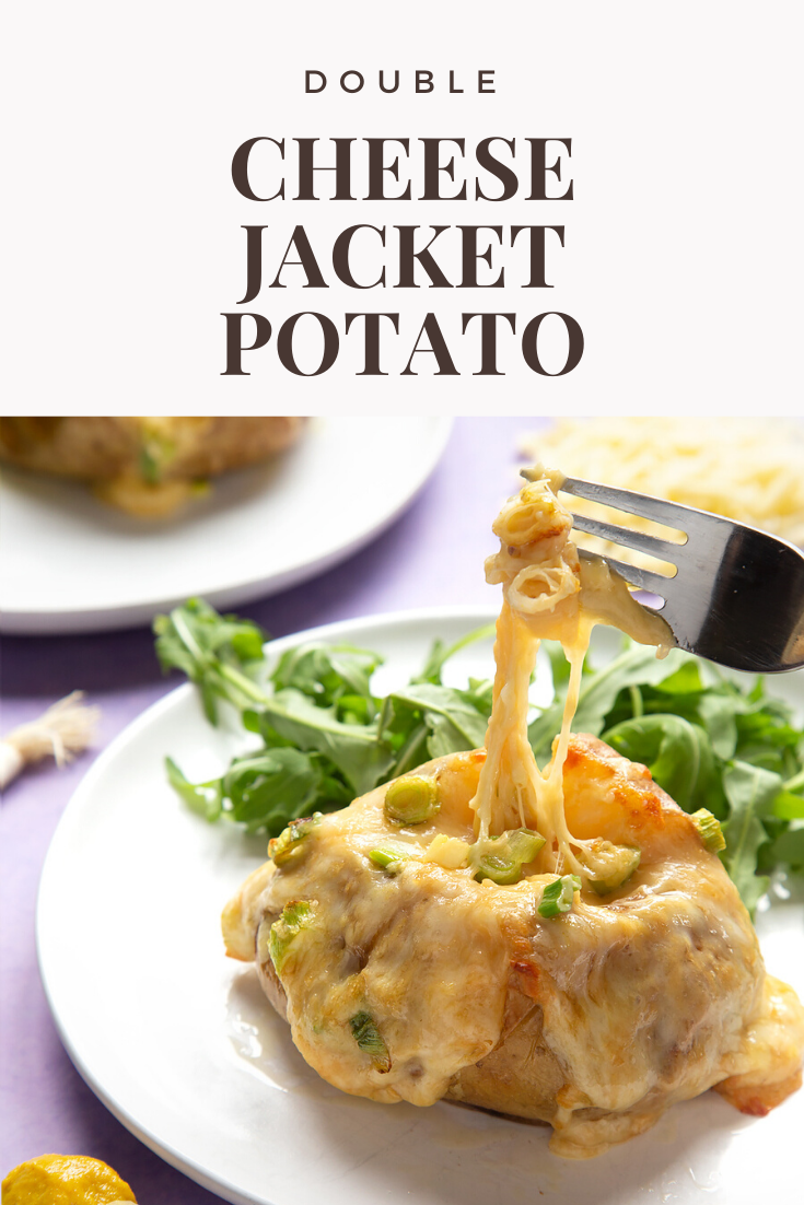 A cheese and onion jacket potato served on a white plate with rocket. A fork lifts the stretchy cheese. Caption reads: double cheese jacket potato