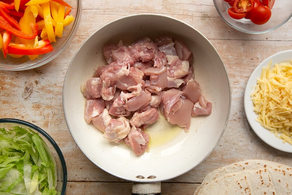 A pan with fried oil  and added chicken, the essential ingredient to Mild chicken fajitas for kids