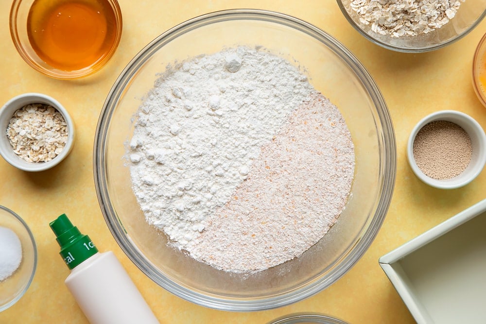 Overhead shot of flour, oats, yeast, and salt in a large clear bowl