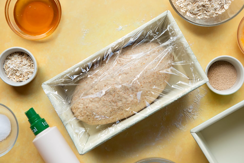 Overhead shot of dough in a loaf tin covered with cling film