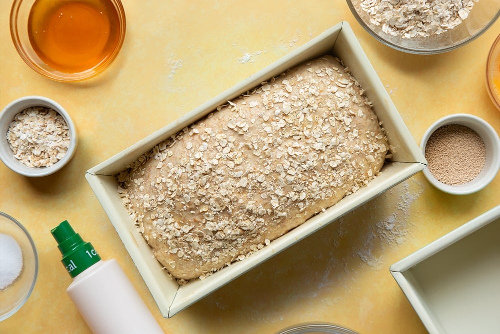 Overhead shot of dough with a sprinkle of oats in a loaf tin