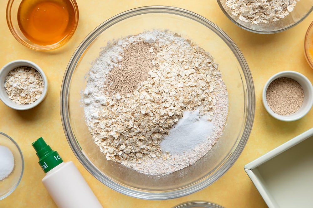 Overhead shot of flour, oats, yeast, and salt in a large clear bowl