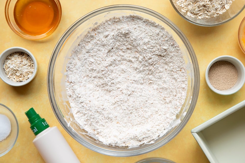 Overhead shot of mixed flour, oats, yeast, and salt in a large clear bowl