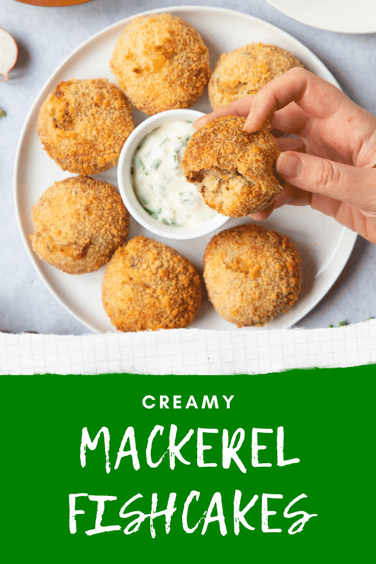 Hand holding a mackerel above a white plate below. On the plate there's a number of additional mackerel fishcakes scatted around a small chive dip. At the bottom of the image there's a green background with some white text describing the image for Pinterest.