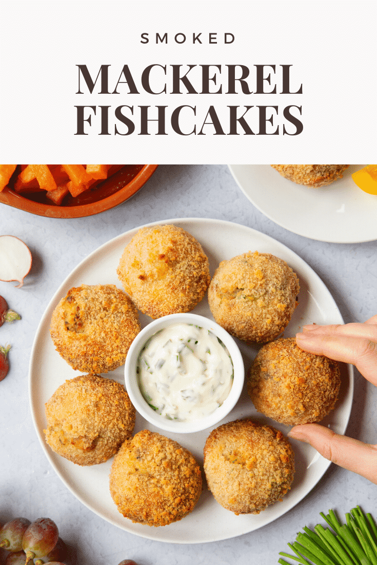 Hand going to pick up the mackerel fishcake from the plate. The plate is sat on a light grey background. At the top of the image there's some text describing the image for Pinterest.