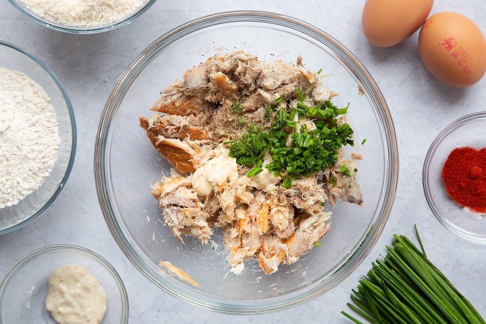 Adding horseradish, chives, salt and pepper to the bowl of mashed mackerel.