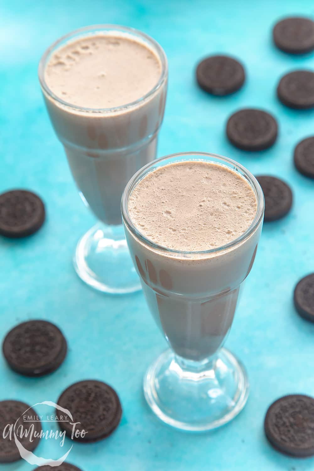 Oreo milkshake ingredients having been blended poured into large milkshake glasses on a light blue background. 