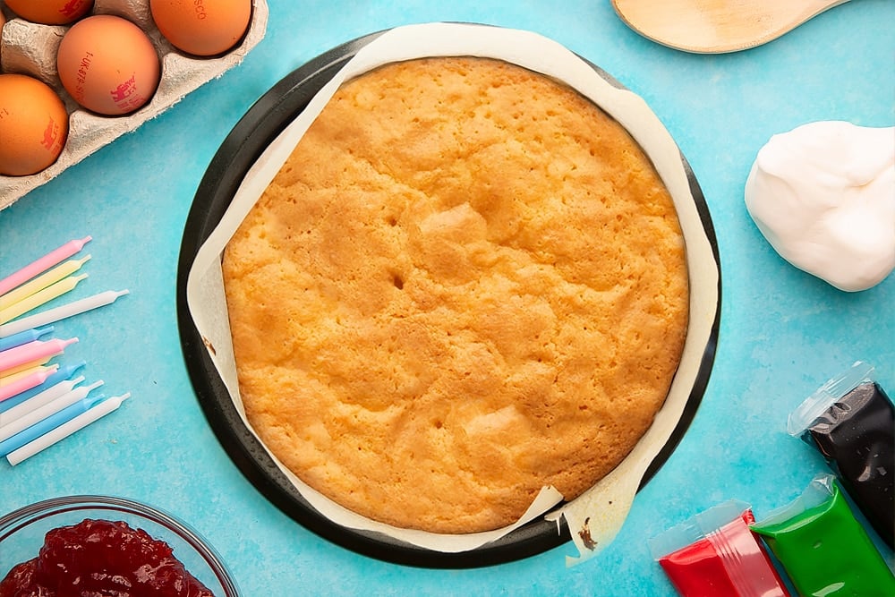 Freshly baked cake in a lined cake tin. Ingredients to make pizza cake surround the tin.
