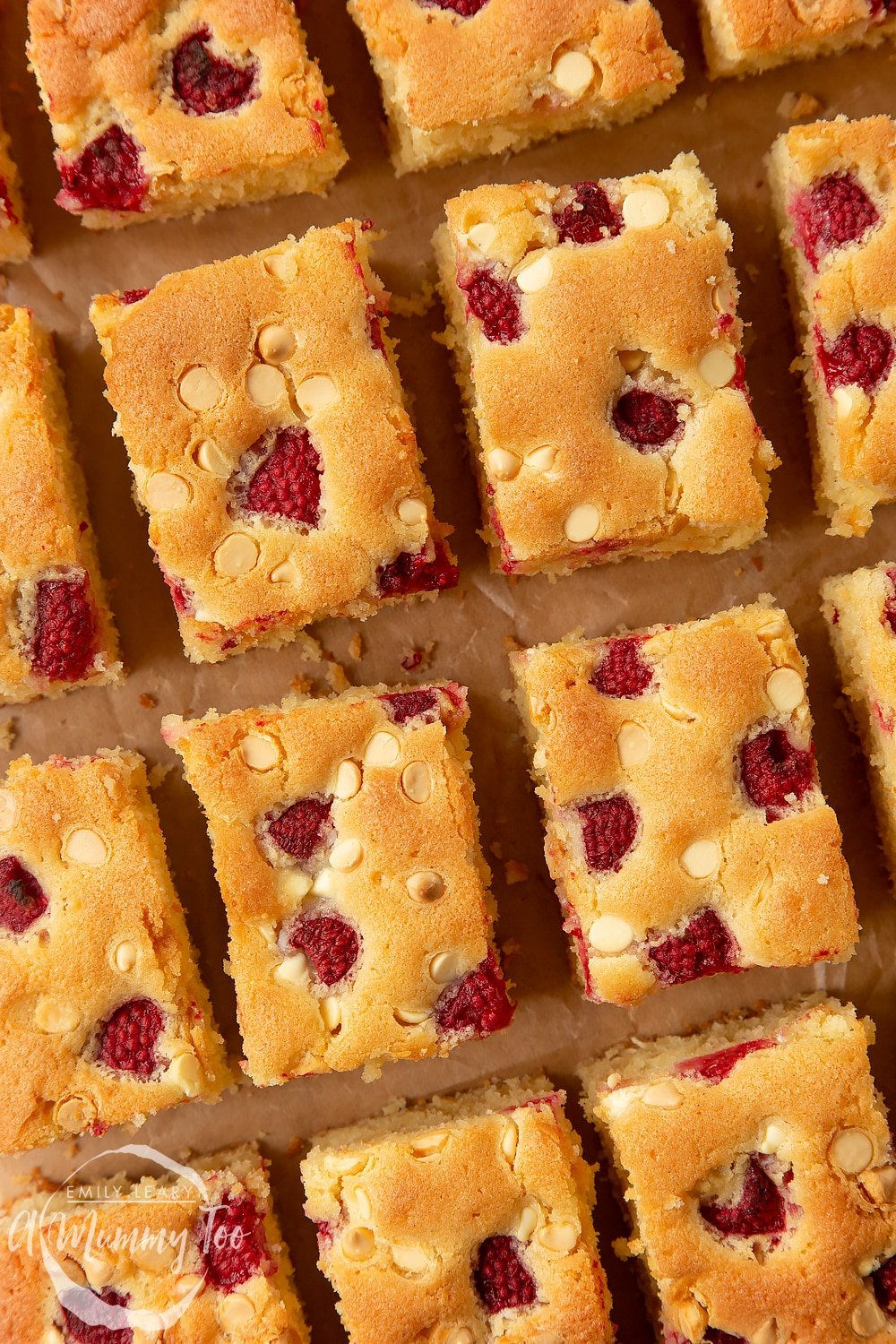 Close up of a raspberry and white chocolate traybake cut into 16 pieces. 