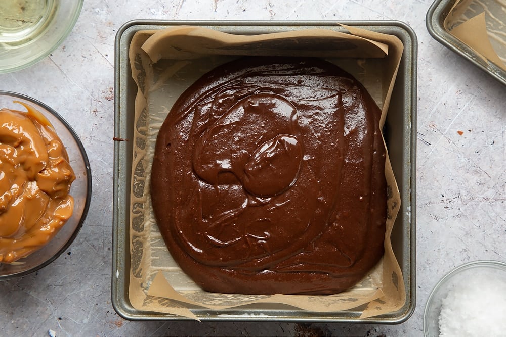 Pouring the gooey salted caramel brownies mixture into a lined cake tin